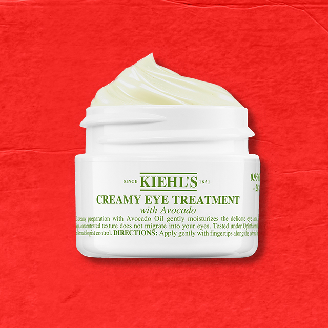 Vasetto bianco di Kiehl’s Creamy Eye Treatment with Avocado aperto, con la crema visibile all’interno, su sfondo rosso testurizzato.