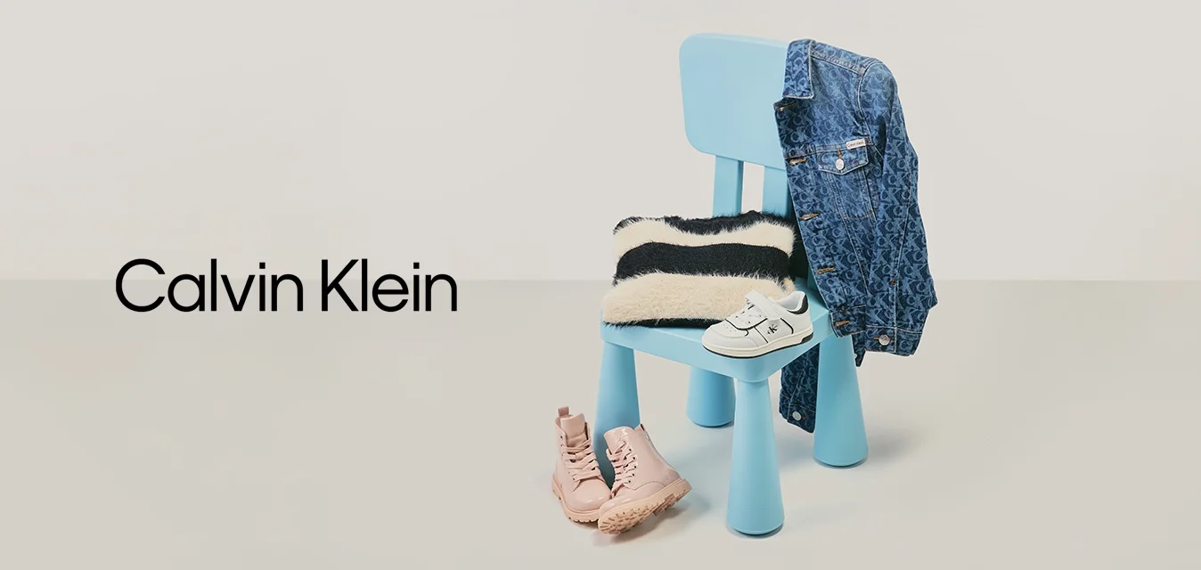 Sedia blu con maglione a righe bianco e nero, giacca di jeans appesa allo schienale, scarpe bianche per bambini sulla seduta e stivali rosa sul pavimento.