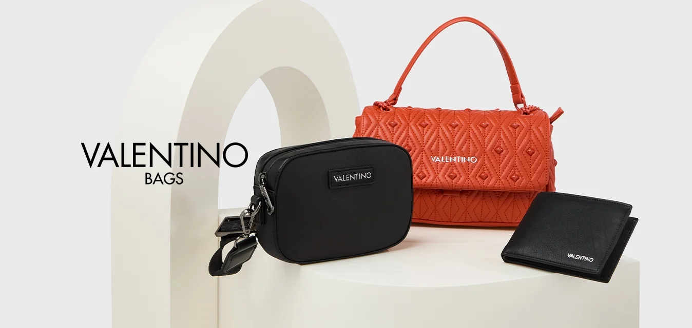 Tre accessori: una borsa arancione strutturata con manico superiore, un piccolo astuccio nero con cerniera e un'etichetta del marchio, e un portafoglio nero, tutti su un piedistallo.