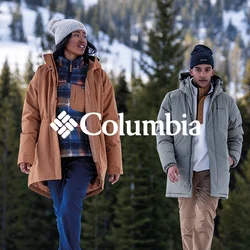 Due persone camminano nella neve, indossando un parka marrone, pantaloni blu, una giacca a vento verde e pantaloni beige. Sullo sfondo si vedono alberi di pino e montagne.