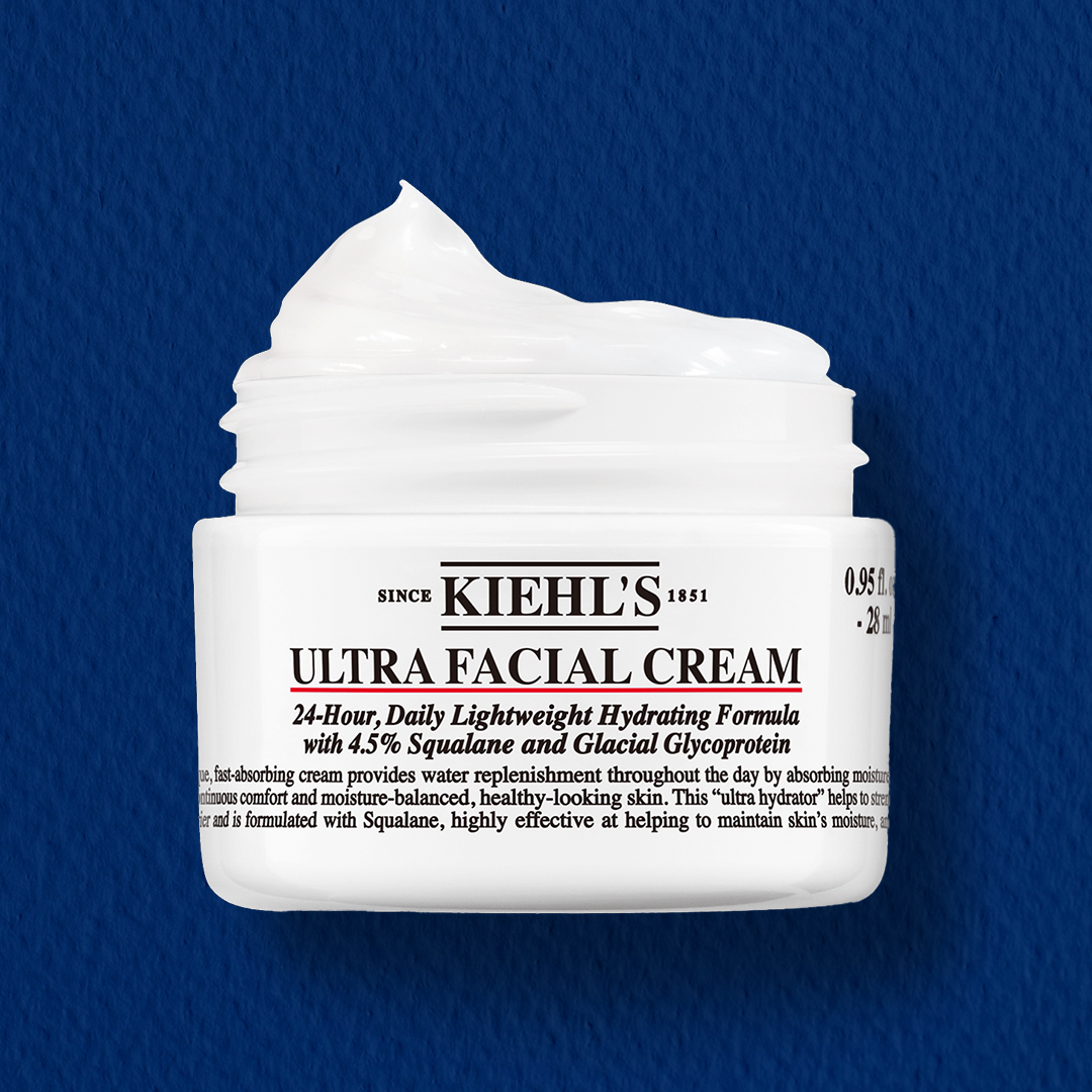 Immagine della crema idratante viso Kiehl’s Ultra Facial Cream, in barattolo bianco da 28 ml, su sfondo blu. Crema leggera con squalano e glicoproteine glaciali per idratazione fino a 24 ore. Questa immagine porta alla scheda prodotto Ultra Facial Cream.