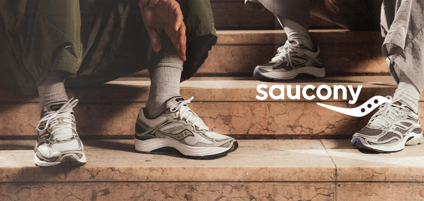 Sneaker bianchi e grigie con pannelli in mesh testurizzati, dettagli neri e lacci bianchi. Indossati con pantaloni grigi e verdi su gradini in pietra.