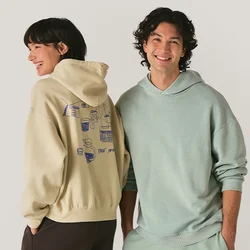 Uomo e donna sorridenti che indossano felpe pastello e pantaloni comodi, in piedi fianco a fianco contro uno sfondo chiaro e semplice.