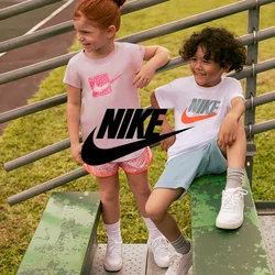 Due bambini siedono su gradini di metallo verdi. La ragazza indossa una maglietta rosa chiaro con un logo Nike rosa e pantaloni corti a fantasia. Il ragazzo indossa una maglietta Nike bianca con un logo arancione e pantaloni corti azzurri.