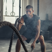 alt="Uomo che si allena con le corde da battaglia in una palestra circondato da una luce nebbiosa, che simboleggia resistenza, energia e potenza.»