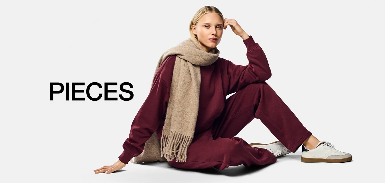 Felpa bordeaux e pantaloni abbinati con vestibilità ampia, abbinati a una sciarpa beige con frange. Sneakers bianche con dettagli color tan.