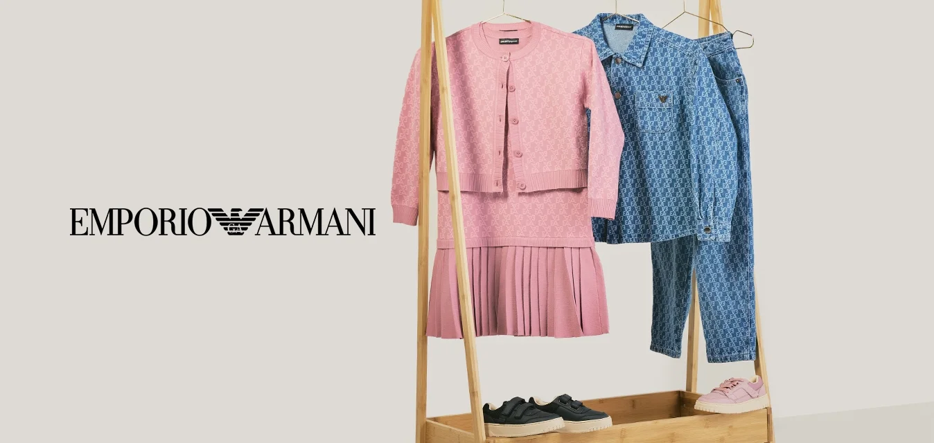 Stendino per abiti in legno con vestito lavorato a maglia rosa e cardigan, camicia blu a fantasia e jeans, sneaker nere e rosa sopra e sotto il rack.