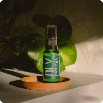 alt="Flacone spray liposomiale con melatonina vitalizzata verde in piedi su un piatto di legno con luce solare soffusa e ombre vegetali dietro di esso.»