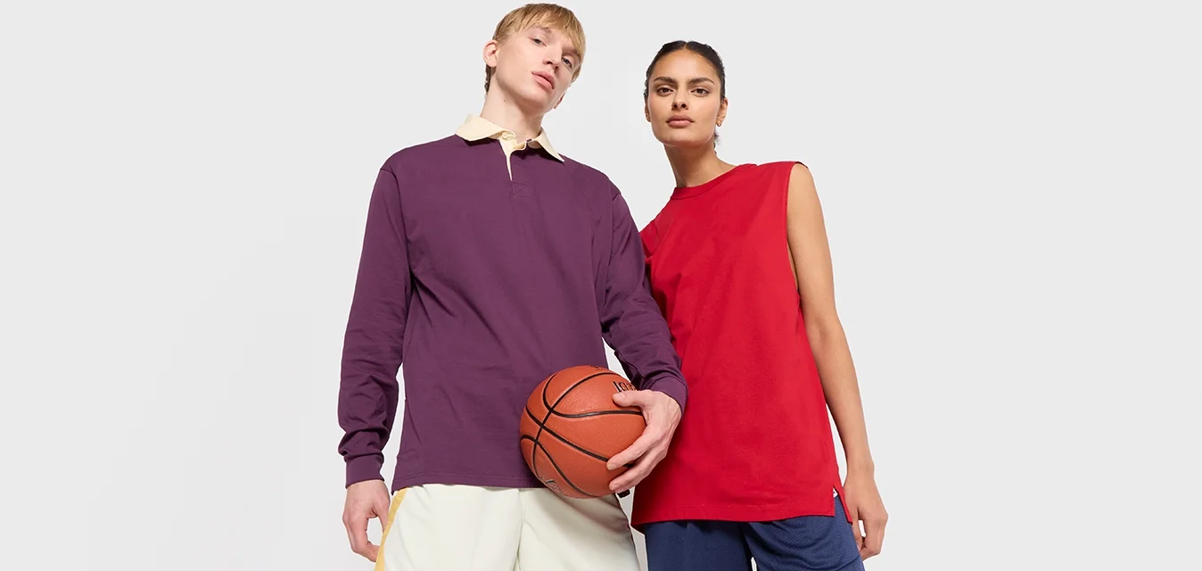 Due persone posano con un pallone da basket. Una indossa un polo a maniche lunghe viola e pantaloni corti crema con strisce gialle; l'altra indossa una canotta rossa e pantaloni corti blu navy.