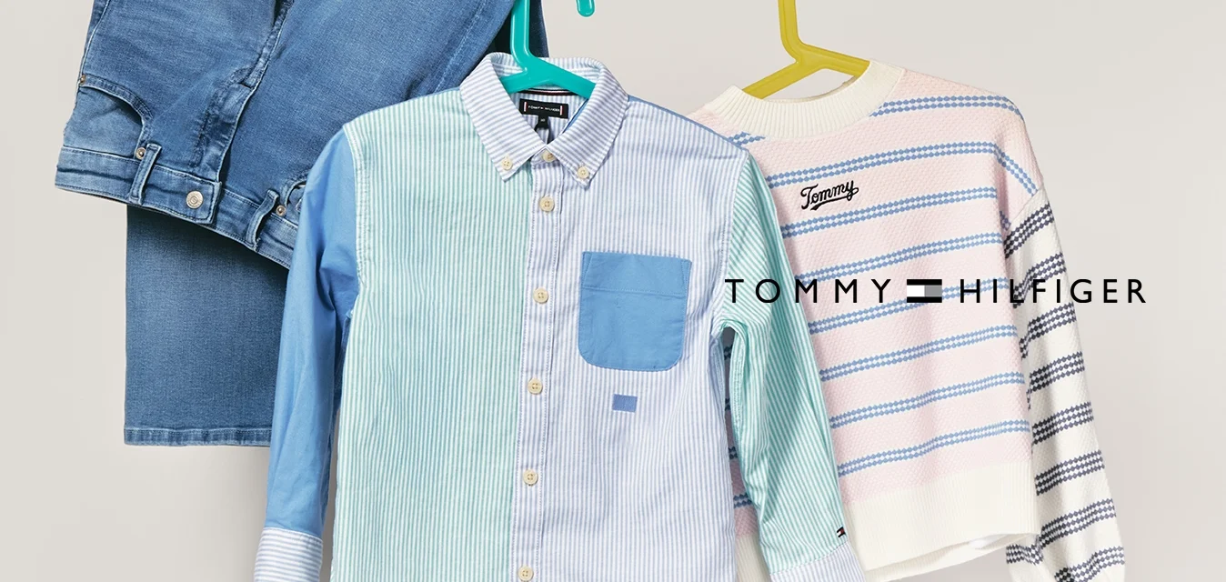 Camicia a righe blu e bianche con taschino blu, appesa accanto a un maglione a righe rosa chiaro e navy e jeans in denim blu.