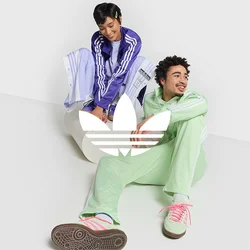 Due persone in abbigliamento sportivo: una in un tuta leggera di colore viola, l'altra in verde menta. Entrambe indossano scarpe da ginnastica casual e sono sedute su una superficie bianca.