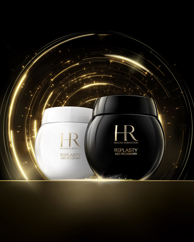 Duo di vasetti di crema Age Recovery Night e Day sono presentati su una superficie dorata con giochi di luce dorati scintillanti su uno sfondo scuro, sottolineando un'estetica premium.