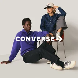 Due persone in abbigliamento casual; una seduta sul pavimento in un maglione viola, pantaloni neri e stivali bianchi; l'altra su sedia in giacca di jeans, pantaloni grigi e cappellino bianco.