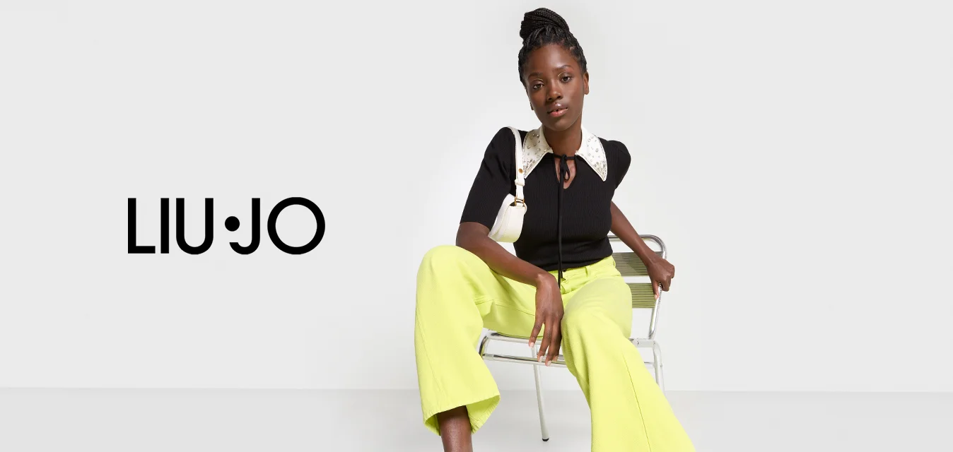 Top nero a costine con colletto bianco decorato e cravattino, abbinato a pantaloni larghi gialli e tacchi neri con straps.