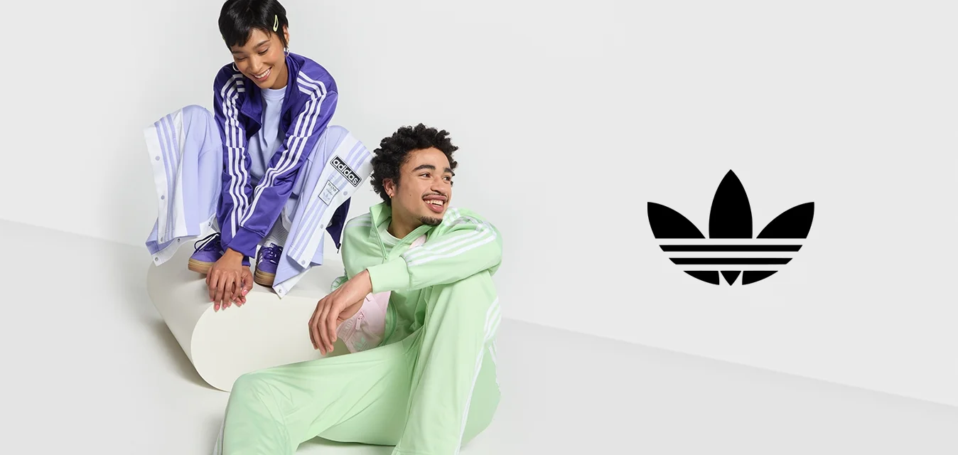 Due persone in abbigliamento sportivo: una in un tuta leggera di colore viola, l'altra in verde menta. Entrambe indossano scarpe da ginnastica casual e sono sedute su una superficie bianca.