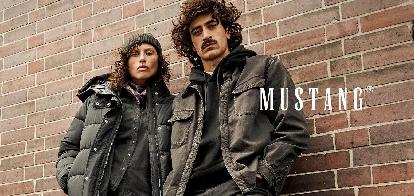 Due persone con abbigliamento casual invernale scuro e stivali appoggiate a un muro di mattoni, una con berretto e giacca imbottita.