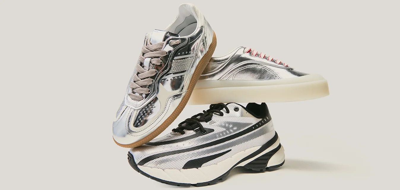 Tre paia di scarpe da ginnastica impilate: tomaia in argento metallizzato, superfici testurizzate, accenti a contrasto in nero e bianco, vari colori e modelli di lacci.