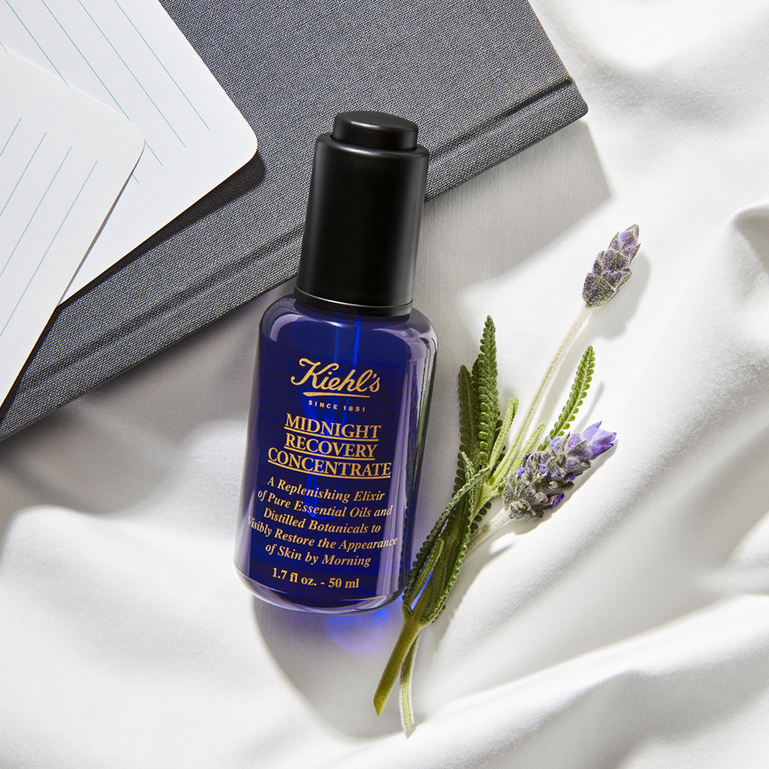 Flacone di Midnight Recovery Concentrate posato su tessuto chiaro con rametti di lavanda accanto.
