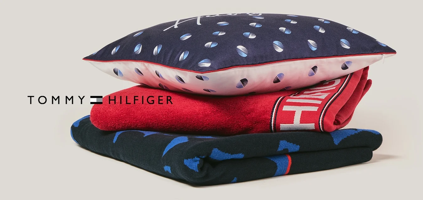 Pila di tre tessuti piegati: tessuto blu con motivo in basso, tessuto rosso con testo bianco al centro, cuscino blu con puntini bianchi e rosa in cima.