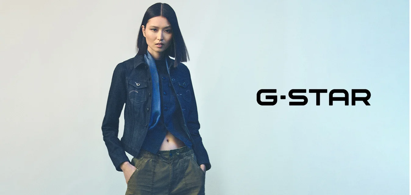 Giacca di jeans dal design aderente, colore blu scuro, con tasche sul davanti, abbinata a una camicia blu con bottoni e pantaloni verde oliva.