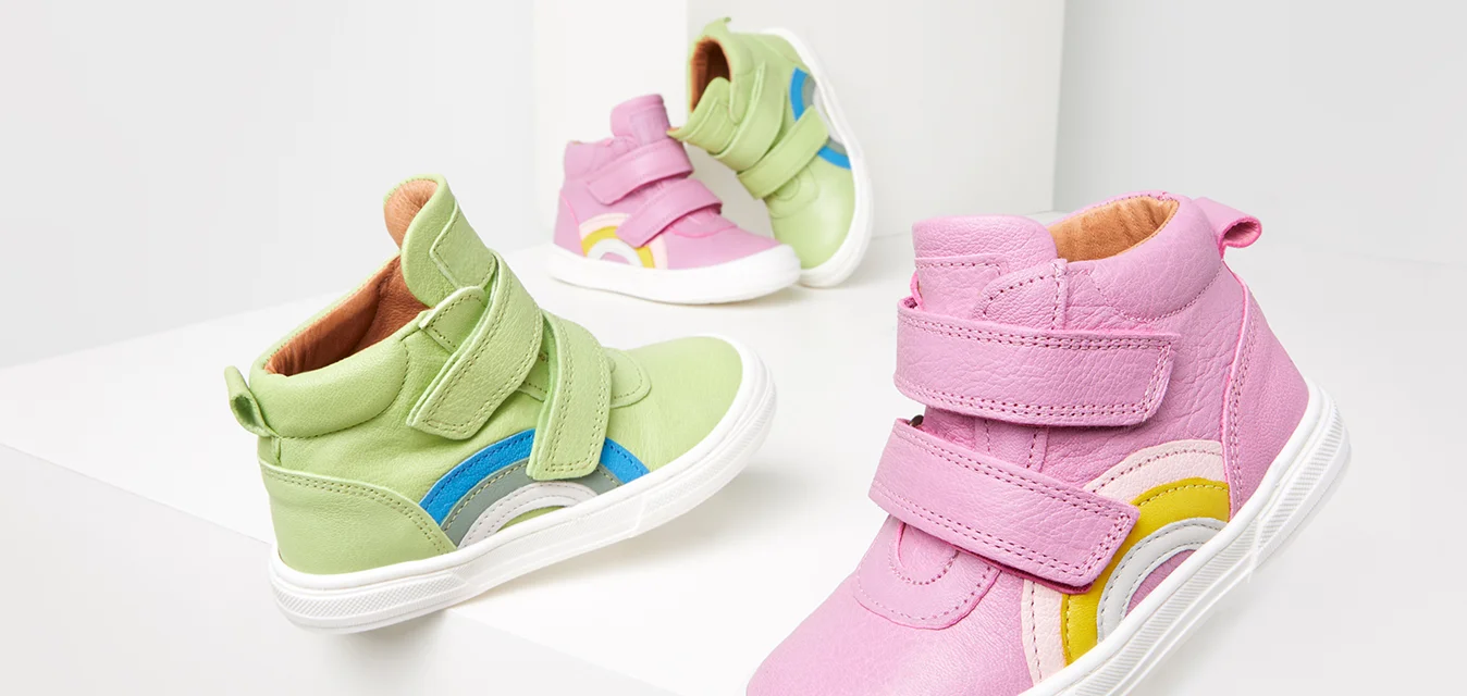 Scarpe alte multicolori per bambini. Una verde con dettagli blu, l'altra rosa con dettagli gialli e bianchi. Entrambe hanno cinturini in velcro.