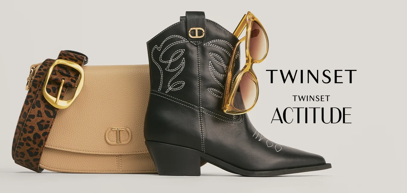 Stivale da cowboy in pelle nera con cuciture bianche, borsa beige con tracolla a stampa leopardata e occhiali da sole con lenti colorate di giallo appoggiati sullo stivale.