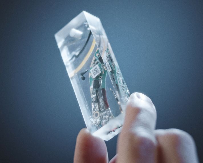 Mano con una capsula a forma di parallelepipedo in resina trasparente con i componenti delle cuffie Dyson OnTrac.