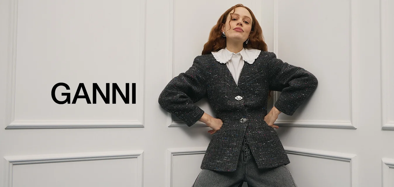 Blazer scuro e strutturato con maniche oversize e dettagli con bottoni argento, abbinato a pantaloni grigi a gamba larga e camicia bianca con colletto.