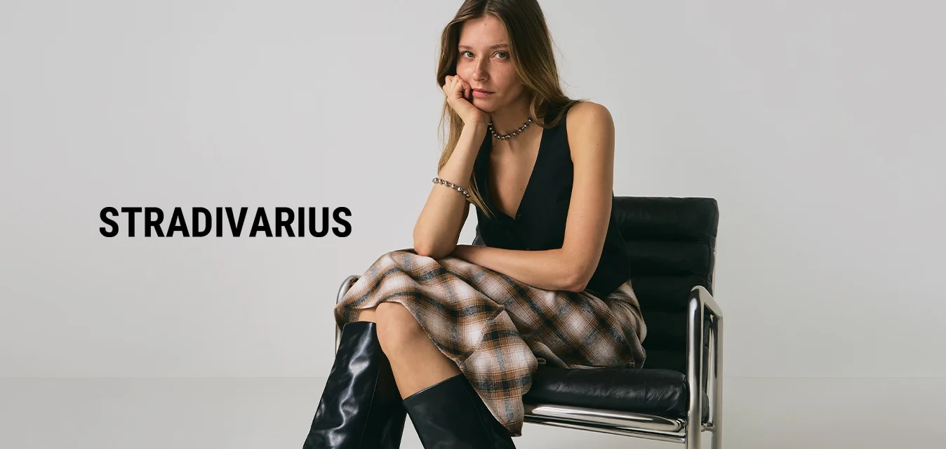 Giovane donna che indossa un top senza maniche nero, una gonna scozzese e stivali neri alti, seduta su una moderna sedia in pelle nera.