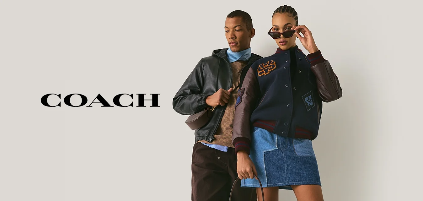 Due modelli posano contro un muro semplice; uno indossa una giacca di pelle, pantaloni marroni e sneaker, l'altro una giacca varsity, una gonna di jeans, stivali e occhiali da sole.