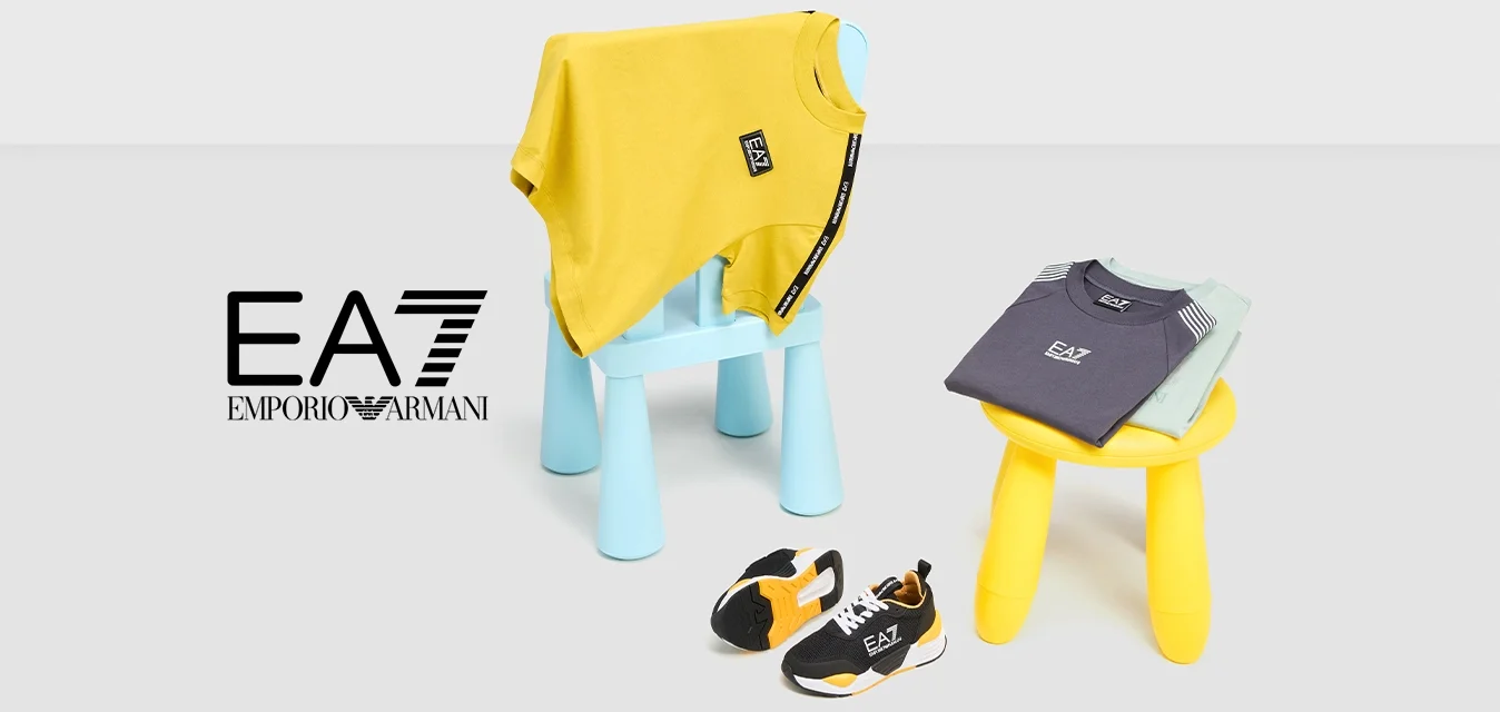 Due magliette per bambini, una gialla e una grigia, esposte su sgabelli colorati. Sneakers nere e arancioni sono posizionate nei pressi sul pavimento.