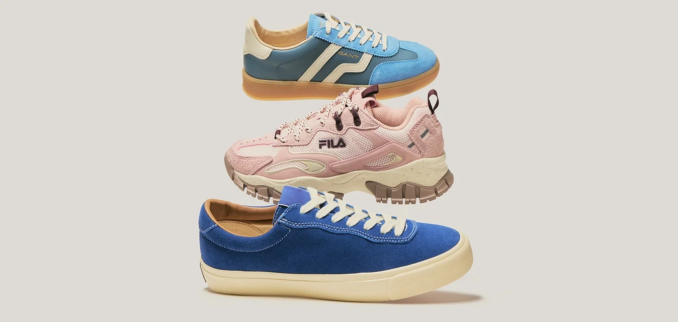 Tre scarpe da ginnastica galleggianti nei colori blu, rosa e blu-grigio su uno sfondo beige uniforme.