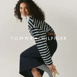 Donna sorridente, sistema un tacco alto beige sopra calzini grigi al ginocchio, indossa un maglione a righe e una gonna blu navy su uno sfondo chiaro e uniforme.