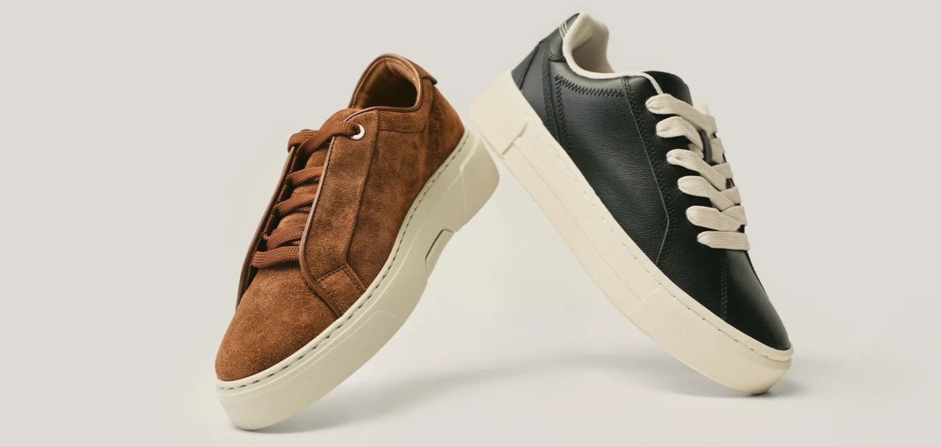 Coppia di sneakers basse casual, una in pelle scamosciata marrone e una in pelle nera, entrambe con suole bianche e lacci abbinati, esposte su uno sfondo chiaro.