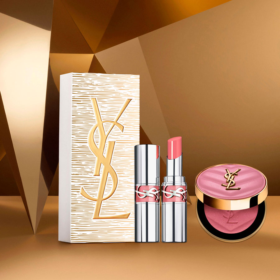 Un set regalo Yves Saint Laurent Beauté con una scatola bianca e oro testurizzata, due balsami o rossetti rosa e un fard rosa scintillante, il tutto su uno sfondo geometrico dorato.