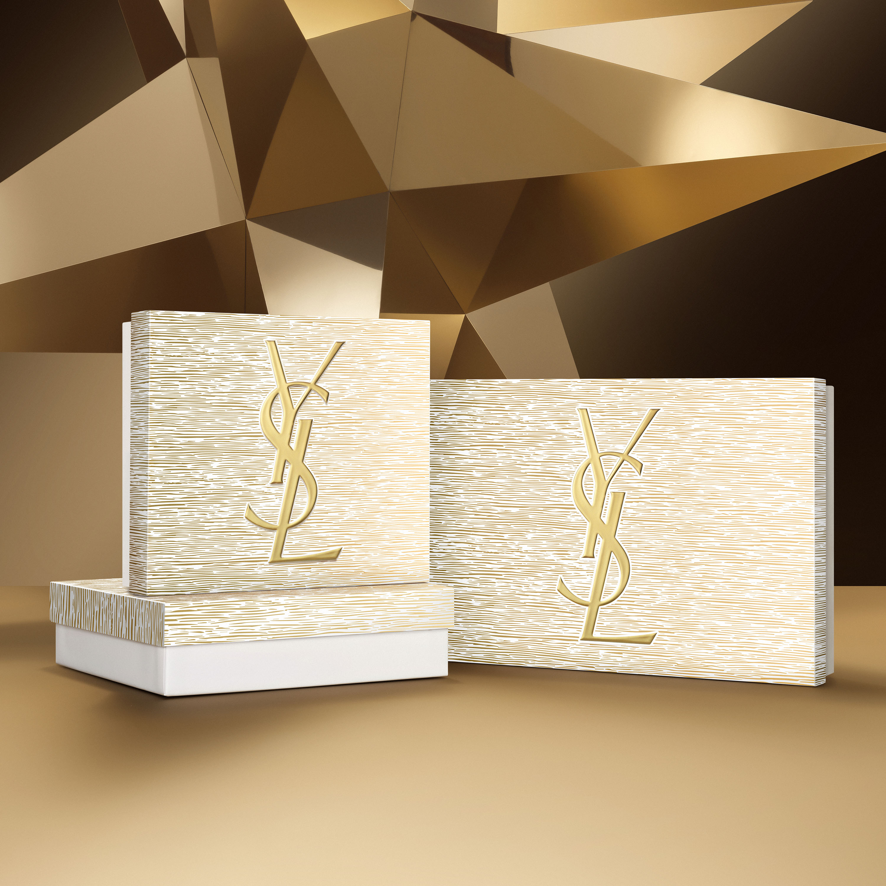 Tre eleganti confezioni regalo Yves Saint Laurent, due più grandi e una più piccola, con un logo YSL dorato e un motivo a strisce testurizzato, su uno sfondo geometrico dorato e scintillante.