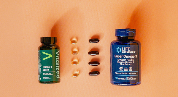 Due integratori di omega-3 presentati su uno sfondo color pesca: Vitalized Omega-3 Vegan a sinistra e Life Extension Super Omega-3 a destra, con le capsule disposte in colonne ordinate tra i flaconi.