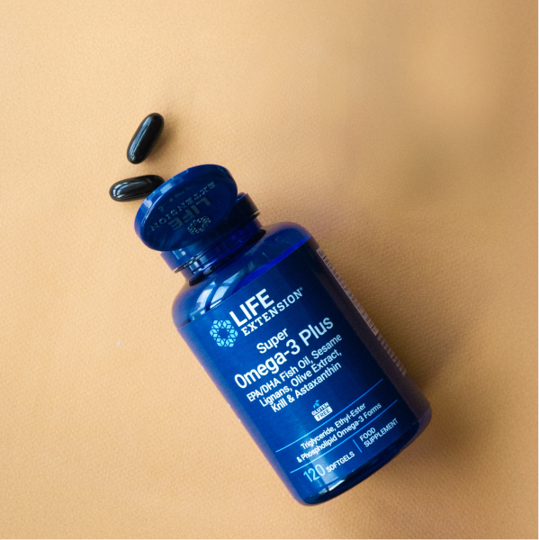 Flacone Life Extension Super Omega-3 Plus adagiato su una superficie marrone chiaro con diverse capsule softgel sparse vicino al coperchio aperto.
