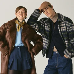 Due persone sono in piedi fianco a fianco indossando cappotti invernali; una indossa un cappotto di shearling marrone e stivali, l'altra un giubbotto fantasia e un berretto.