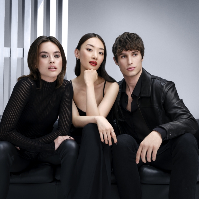 Tre individui diversi, due donne e un uomo, vestiti di nero, sono seduti con sicurezza su un divano in pelle scura.