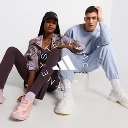 Due modelli seduti su una superficie chiara. Uno indossa un giacca marrone a fantasia, leggings viola e scarpe da ginnastica rosa. L'altro indossa un tuta blu chiaro e scarpe da ginnastica bianche.