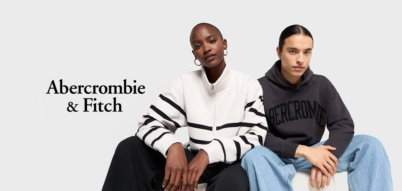 Due modelli seduti uno accanto all'altro. Uno indossa una felpa bianca con cerniera e strisce nere, l'altro una felpa scura con la scritta 