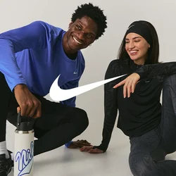 Due persone in abbigliamento sportivo sedute a terra, sorridenti; una tiene una bottiglia d'acqua, entrambe sembrano rilassate e amichevoli.