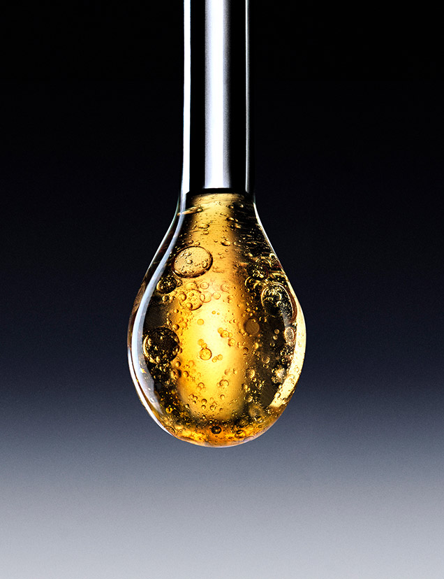 Primo piano artistico su una pipetta di vetro che rilascia una goccia dorata e preziosa, illustrando la formula concentrata in Pro-Xylane TM. La goccia brilla su uno sfondo scuro sfumato, evidenziando la ricchezza di questo ingrediente anti-invecchiamento brevettato.