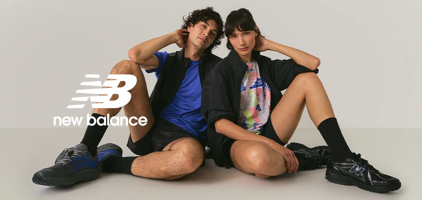 Due giovani adulti seduti per terra con le gambe piegate, vestiti con abbigliamento sportivo casual e scarpe da ginnastica, su uno sfondo chiaro e semplice.