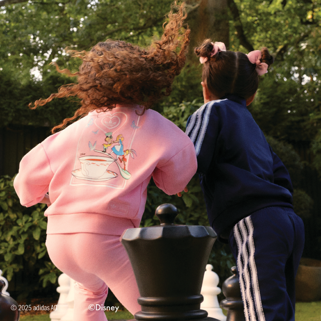 Two girls running. One wears a pink sweater and leggings, the other is in a blue tracksuit