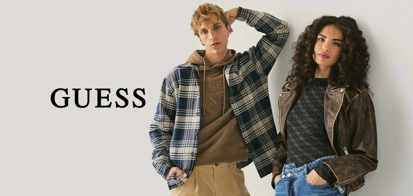 Due giovani adulti appoggiati a un muro, vestiti con abiti casual autunnali: giacca a quadri, felpa con cappuccio, pantaloni kaki e giacca di pelle con jeans.