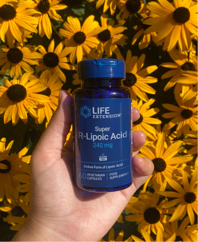 Tenendo in mano una bottiglia di Life Extension Super R-Lipoic Acid davanti a fiori gialli.