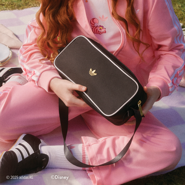 Girl sitting on a blanket in pink tracksuit holiding a black bag