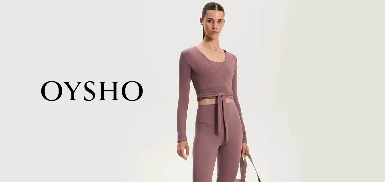 Top corto sportivo in malva con chiusura a fiocco, abbinato a leggings a vita alta; il modello tiene una borsa da viaggio color taupe coordinata; sneakers con dettagli crema.